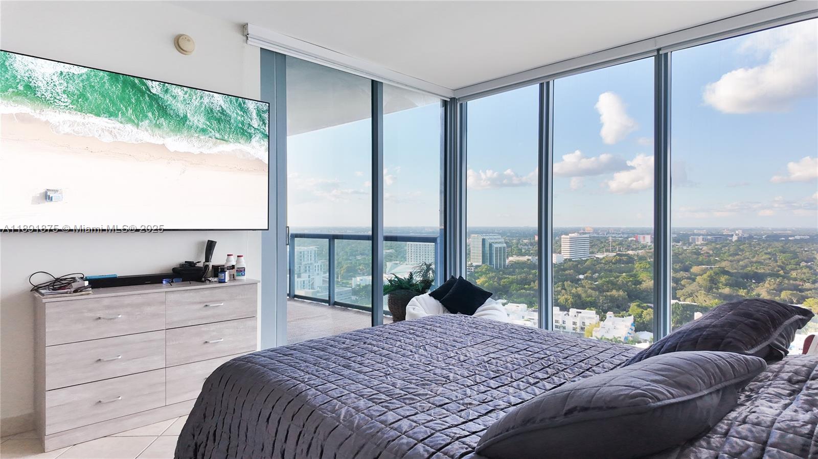 A bedroom features a bed, a dresser with a television, and floor-to-ceiling windows overlooking cityscapes — 601 NE 36th St # 2206, Miami FL 33137, MIAMI, FL