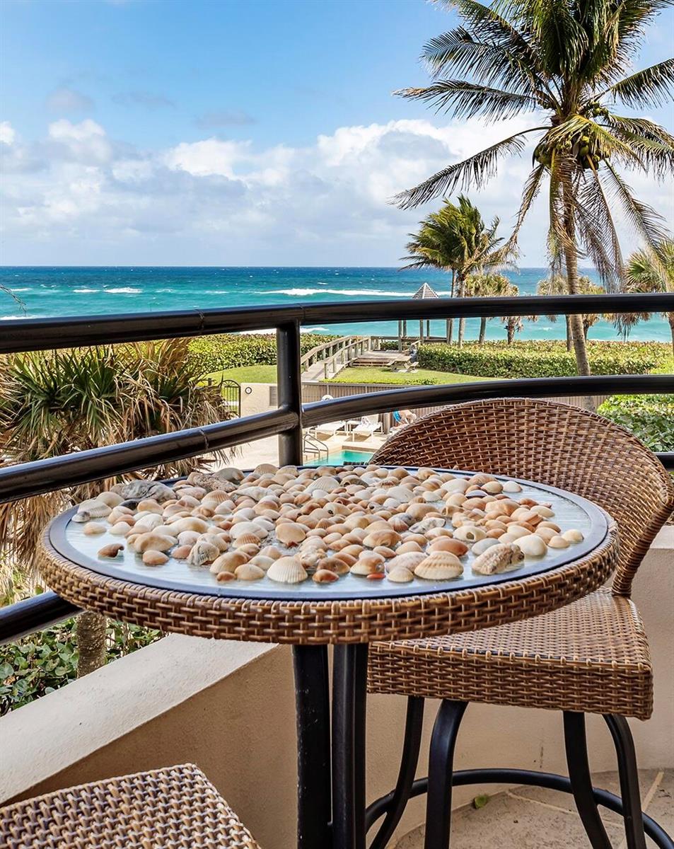 A balcony features a table covered in seashells overlooking a swimming pool and the ocean — 420 Celestial Way # 301, Juno Beach FL 33408, JUNO BEACH, FL