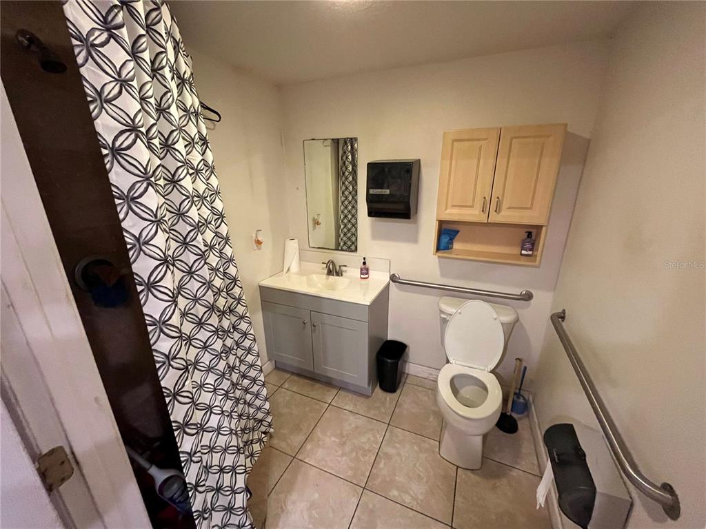 A bathroom features a gray vanity, a toilet with grab bars, and a patterned shower curtain — 177 US HIGHWAY 27 S, SEBRING, FL