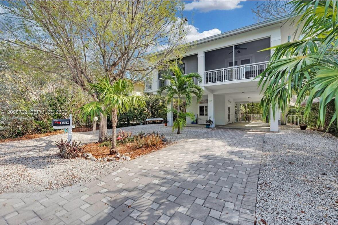 A two-story house with a screened-in balcony and a paved driveway sits on gravel landscaping — 1019 Snapper Ln, Key Largo FL 33037, KEY LARGO, FL