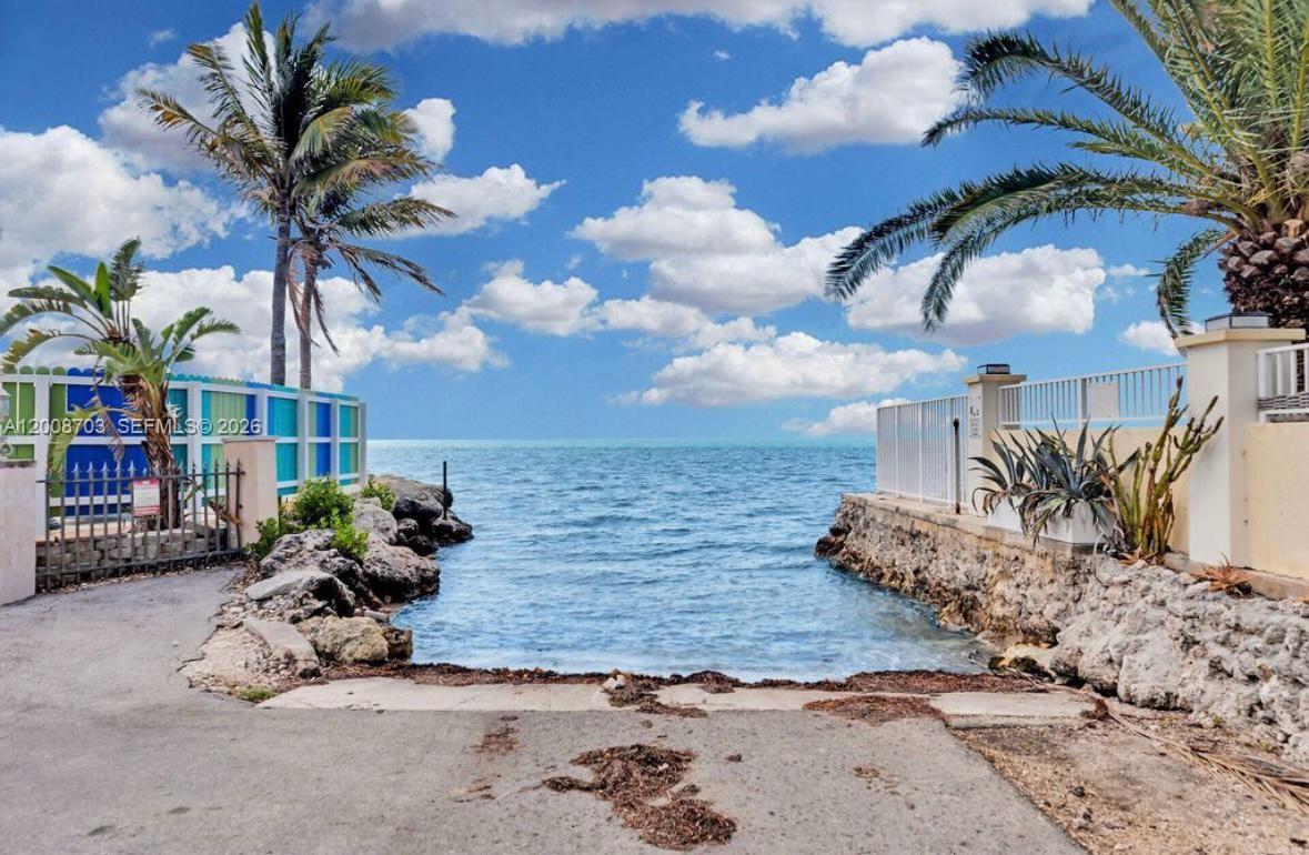 A paved path leads to a small water access point framed by palm trees and rocks — 1019 Snapper Ln, Key Largo FL 33037, KEY LARGO, FL