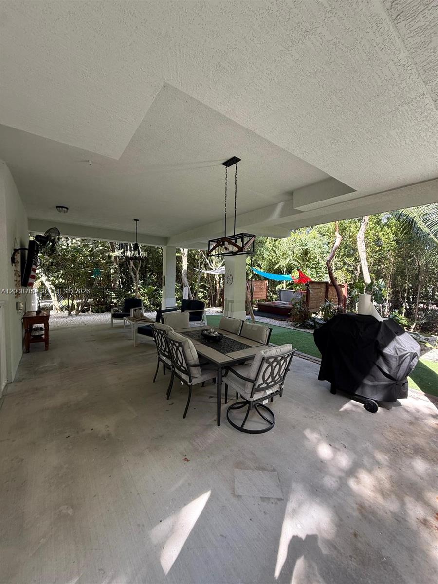 A covered patio features a dining set, a grill, and a view of the backyard — 1019 Snapper Ln, Key Largo FL 33037, KEY LARGO, FL
