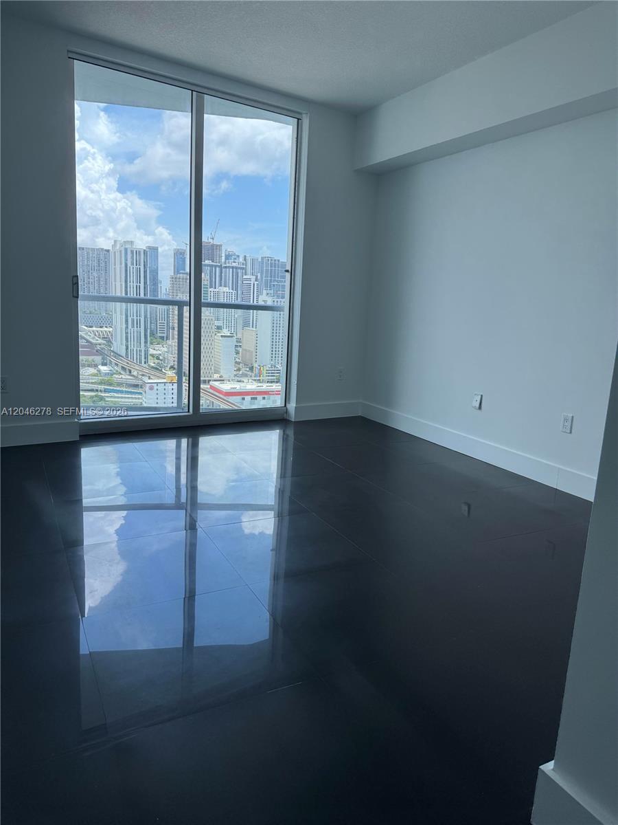 An empty room features dark tile flooring, white walls, and floor-to-ceiling windows overlooking a city — 185 SW 7th St # 3009, Miami FL 33130, MIAMI, FL
