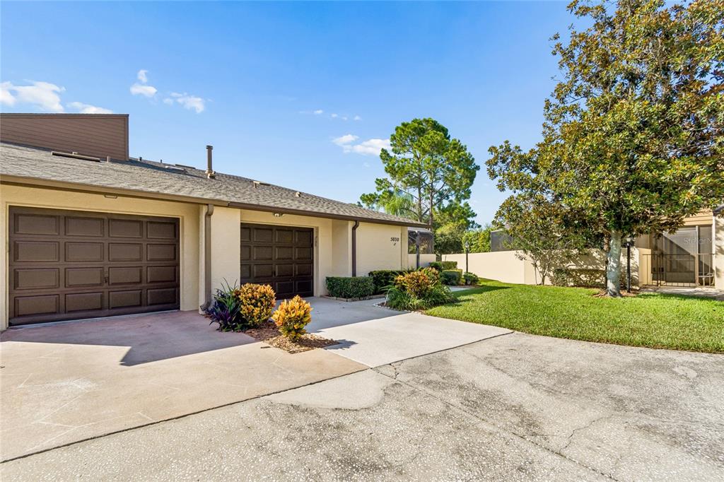 A single-story residential building with two garage doors, a concrete driveway, and surrounding landscaping — 5030 UMBER WAY N, TAMPA, FL