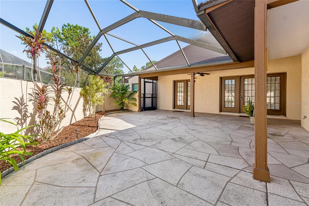 A screened-in patio features a patterned concrete floor, tan stucco walls, and tropical landscaping — 5030 UMBER WAY N, TAMPA, FL