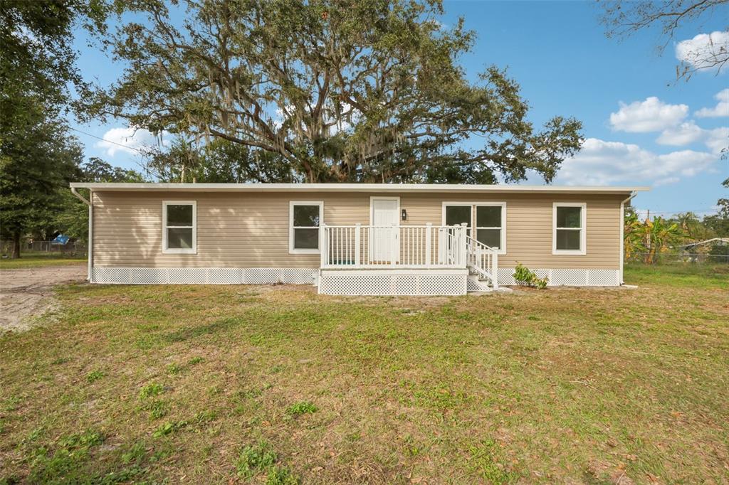 A single-story manufactured home with tan siding and a white front deck under a tree — 1427 COMBEE LANE, LAKELAND, FL