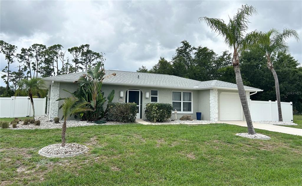A single-story house with a light-colored exterior, a garage, and palm trees in the yard — 2477 CANNOLOT BOULEVARD, PORT CHARLOTTE, FL