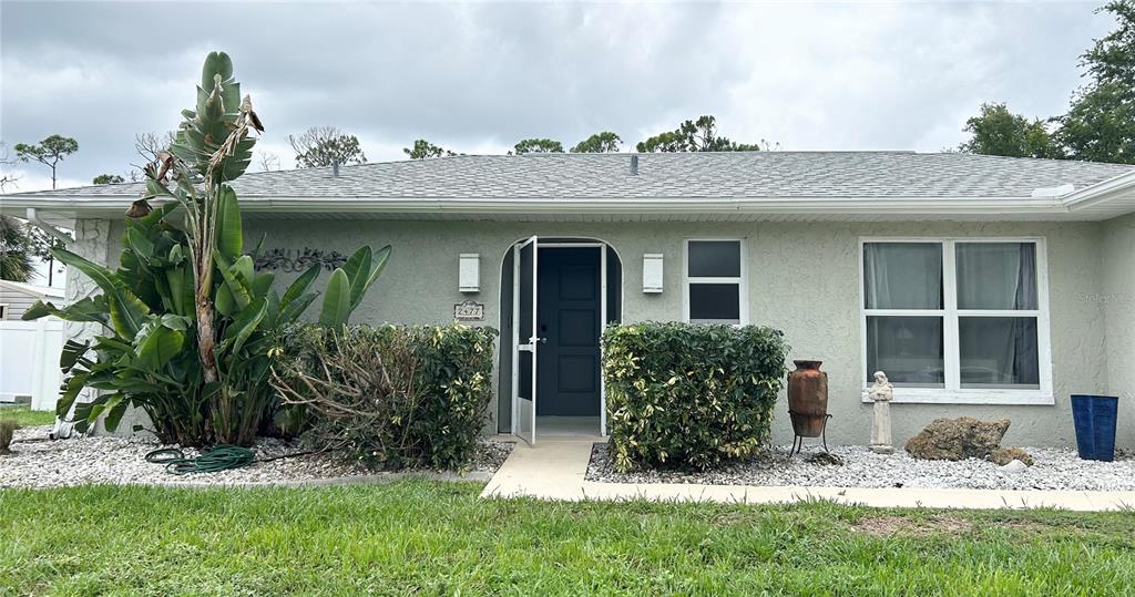 The exterior of a single-story house features a light-colored facade, a front door, and landscaping — 2477 CANNOLOT BOULEVARD, PORT CHARLOTTE, FL
