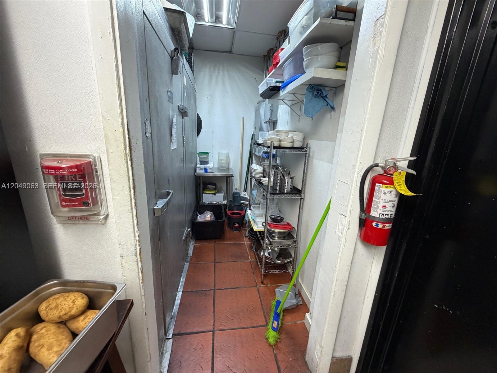 A narrow commercial kitchen storage area features a walk-in cooler, metal shelving, and tile flooring — Restaurant space NW For Lease, Miami FL 33122, MIAMI, FL