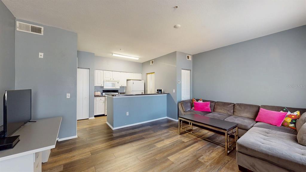 A living room with wood-look flooring, gray walls, and an open kitchen with white cabinets — 10764 70TH AVENUE UNIT 2208, SEMINOLE, FL