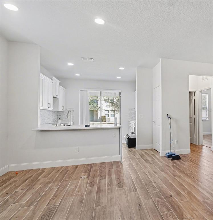 A kitchen with white cabinets and a breakfast bar overlooks a room with wood-look flooring — 406 CAPRON ASH LOOP, CASSELBERRY, FL
