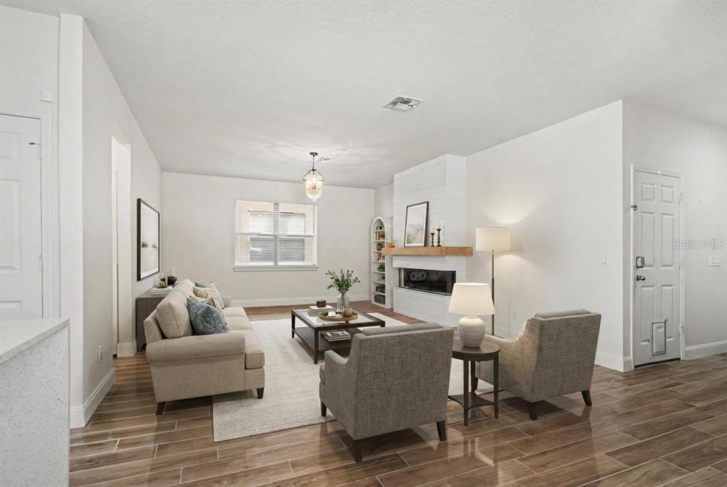 A living room features a white fireplace, beige sofa, two gray armchairs, and wood-look flooring — 406 CAPRON ASH LOOP, CASSELBERRY, FL