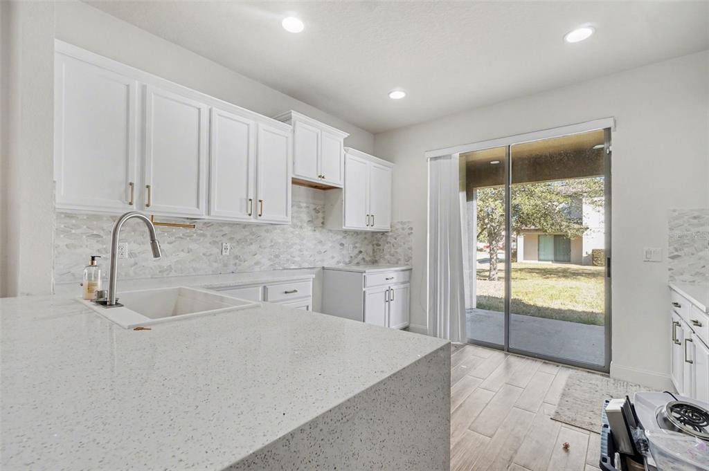 A kitchen with white cabinets, quartz countertops, a tile backsplash, and a sliding glass door — 406 CAPRON ASH LOOP, CASSELBERRY, FL