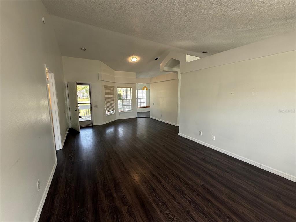 An empty living room features dark wood-look flooring, white walls, and a vaulted ceiling — 13102 LINDEN DRIVE, SPRING HILL, FL