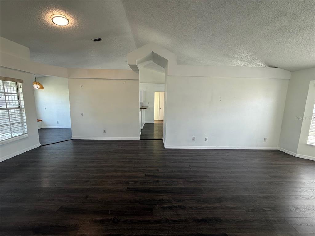 A spacious living area features dark wood-look flooring, white walls, and a vaulted ceiling — 13102 LINDEN DRIVE, SPRING HILL, FL