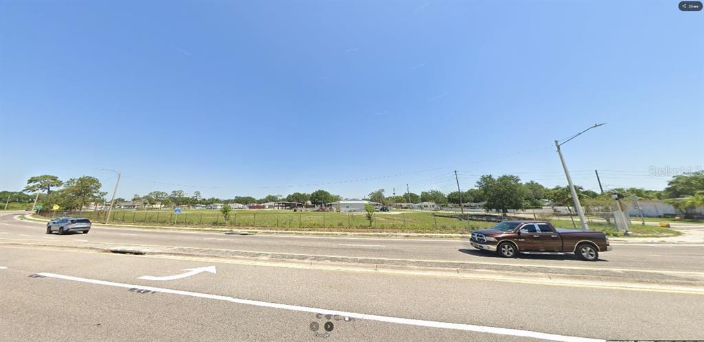 A brown pickup truck drives past a large, fenced-in vacant lot on a sunny day — HWY 60 E, LAKE WALES, FL