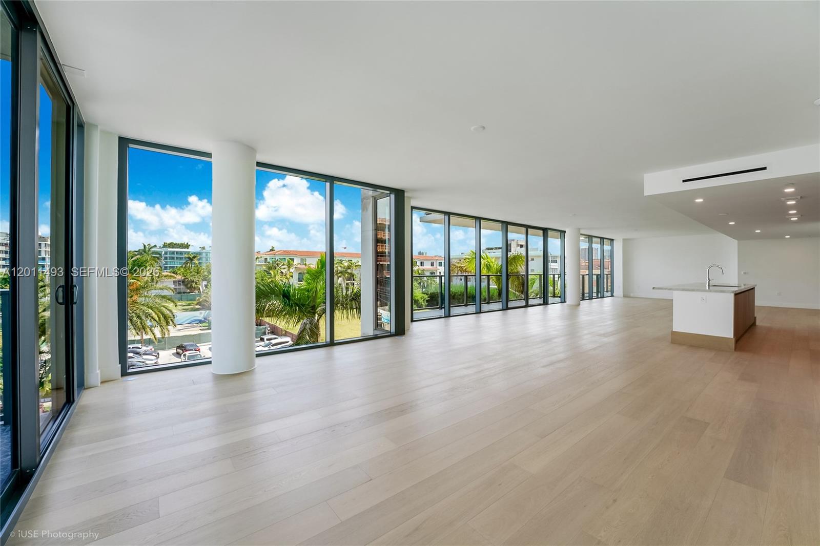 An open-concept living area features light wood flooring, floor-to-ceiling windows, and a kitchen island — 1177 Kane Concourse # 405, Bay Harbor Islands FL 33154, BAY HARBOR ISLANDS, FL