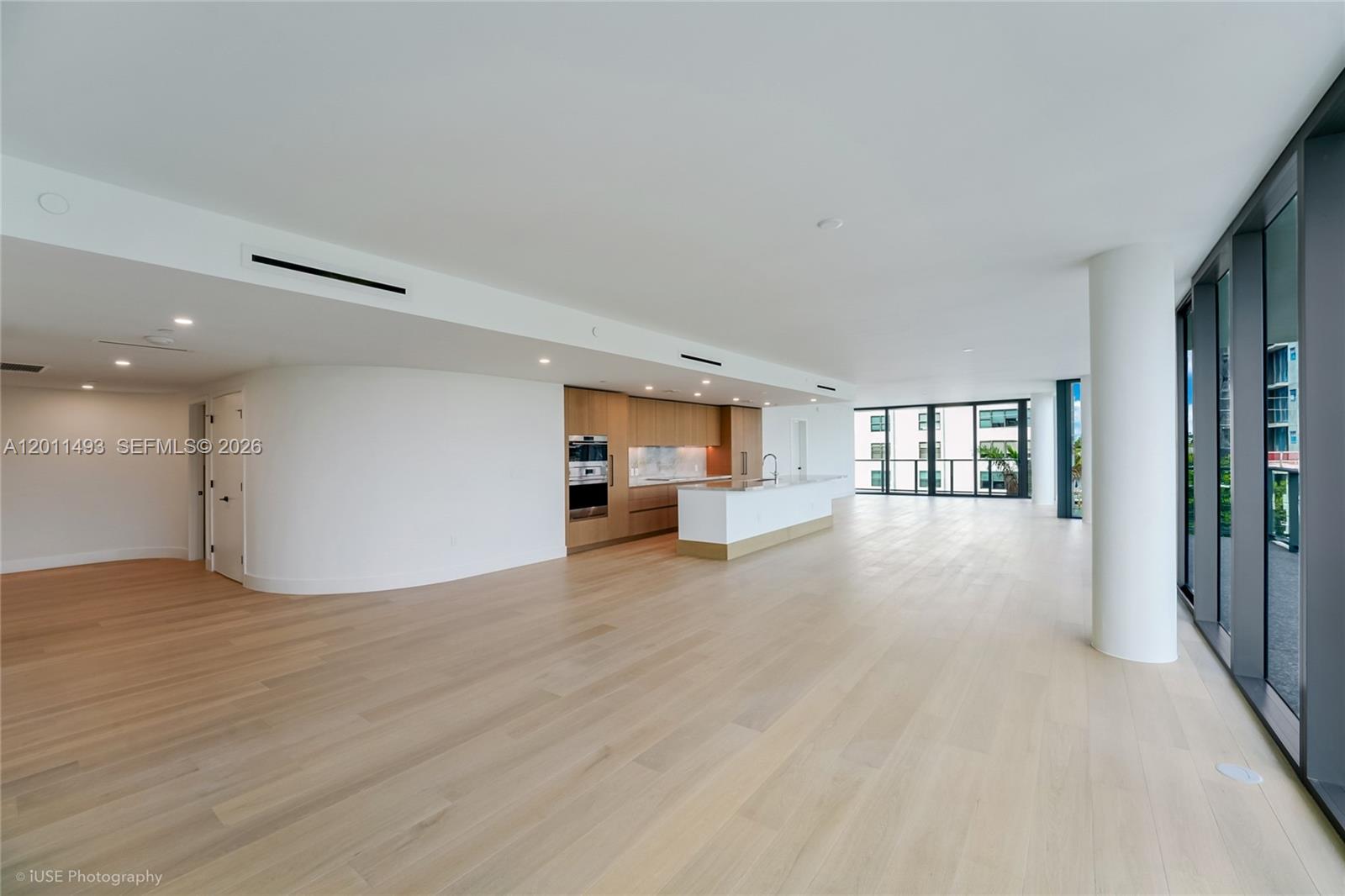 An open-concept kitchen with light wood cabinetry and a white island overlooks a spacious room — 1177 Kane Concourse # 405, Bay Harbor Islands FL 33154, BAY HARBOR ISLANDS, FL
