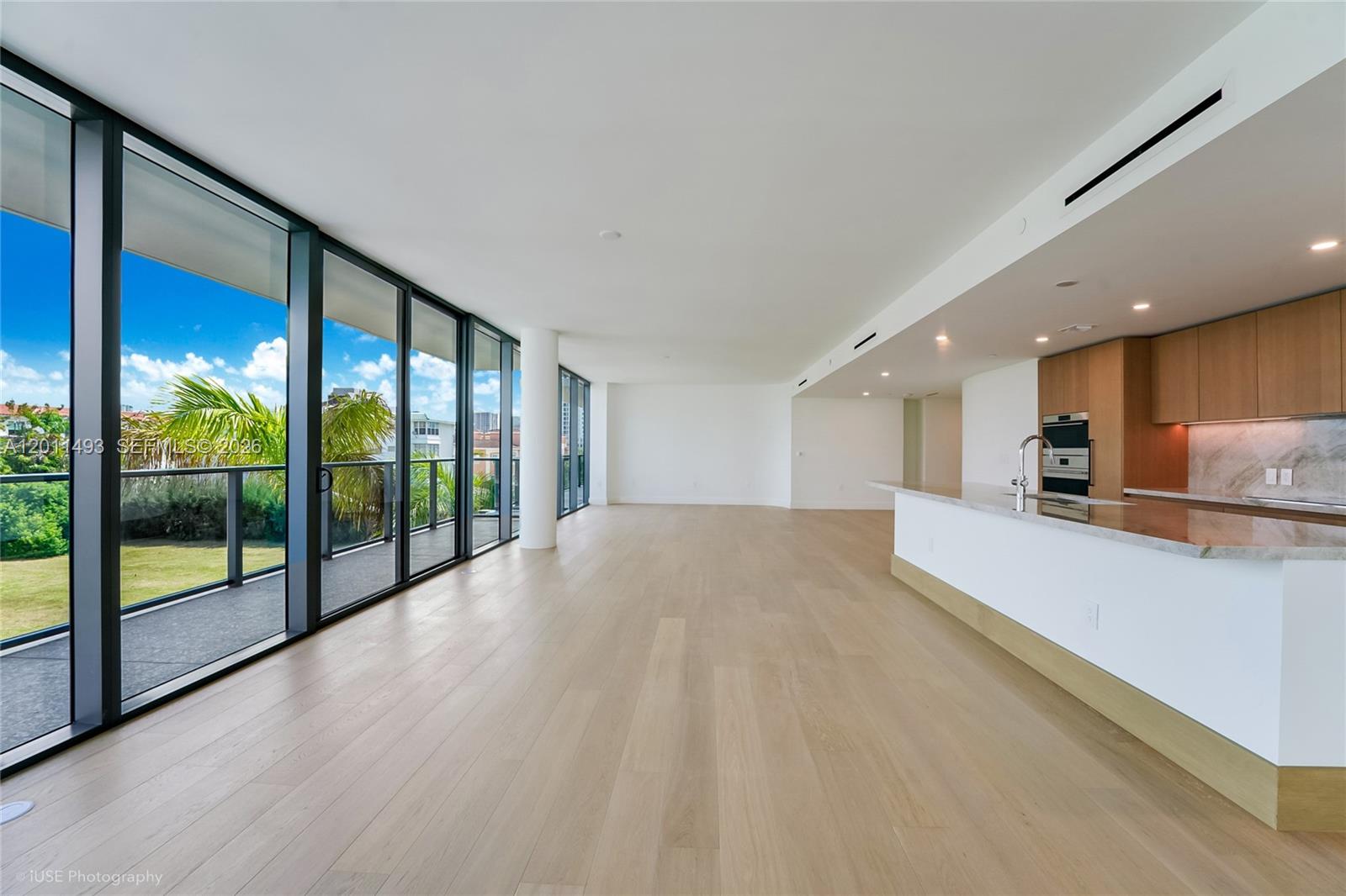 An open-concept living area features light wood floors, a modern kitchen, and floor-to-ceiling windows — 1177 Kane Concourse # 405, Bay Harbor Islands FL 33154, BAY HARBOR ISLANDS, FL