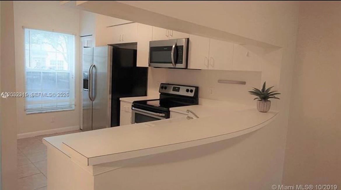 A kitchen features stainless steel appliances, white cabinetry, and light-colored tile flooring — 1 Simonton Cir # 1, Weston FL 33326, WESTON, FL