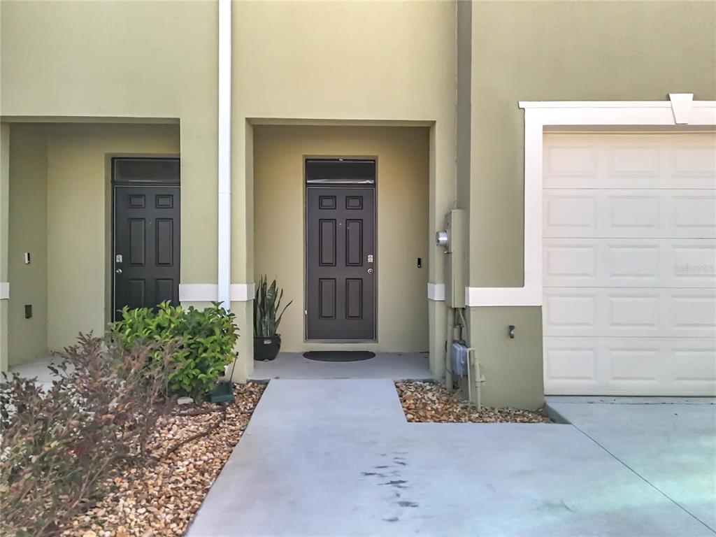 The exterior of a townhouse features two dark front doors, a garage, and landscaping — 965 LIDO DRIVE, HOWEY IN THE HILLS, FL