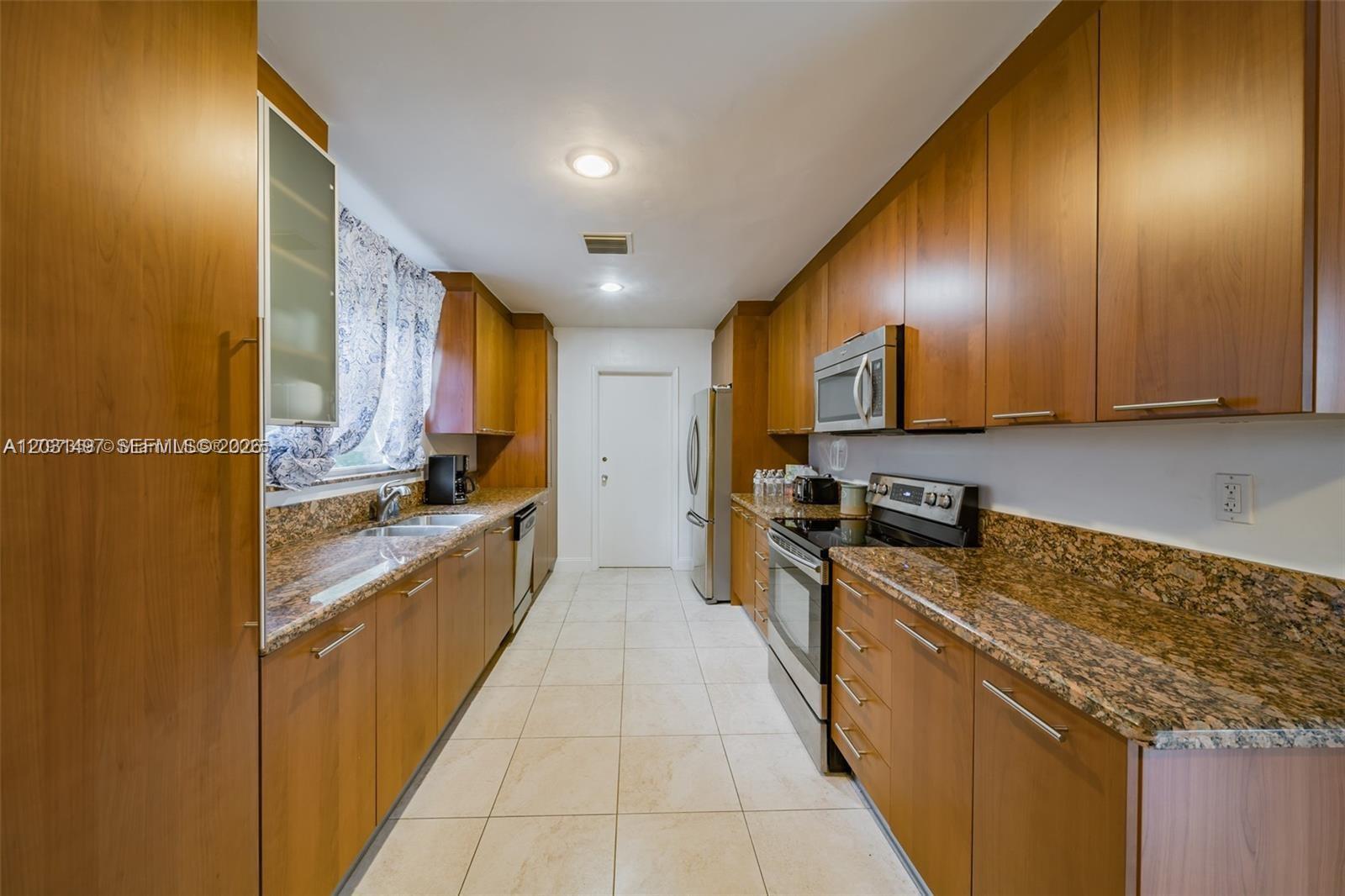 A galley kitchen features wood cabinets, granite countertops, stainless steel appliances, and light tile flooring — 4410 N Buchanan St, Hollywood FL 33021, HOLLYWOOD, FL