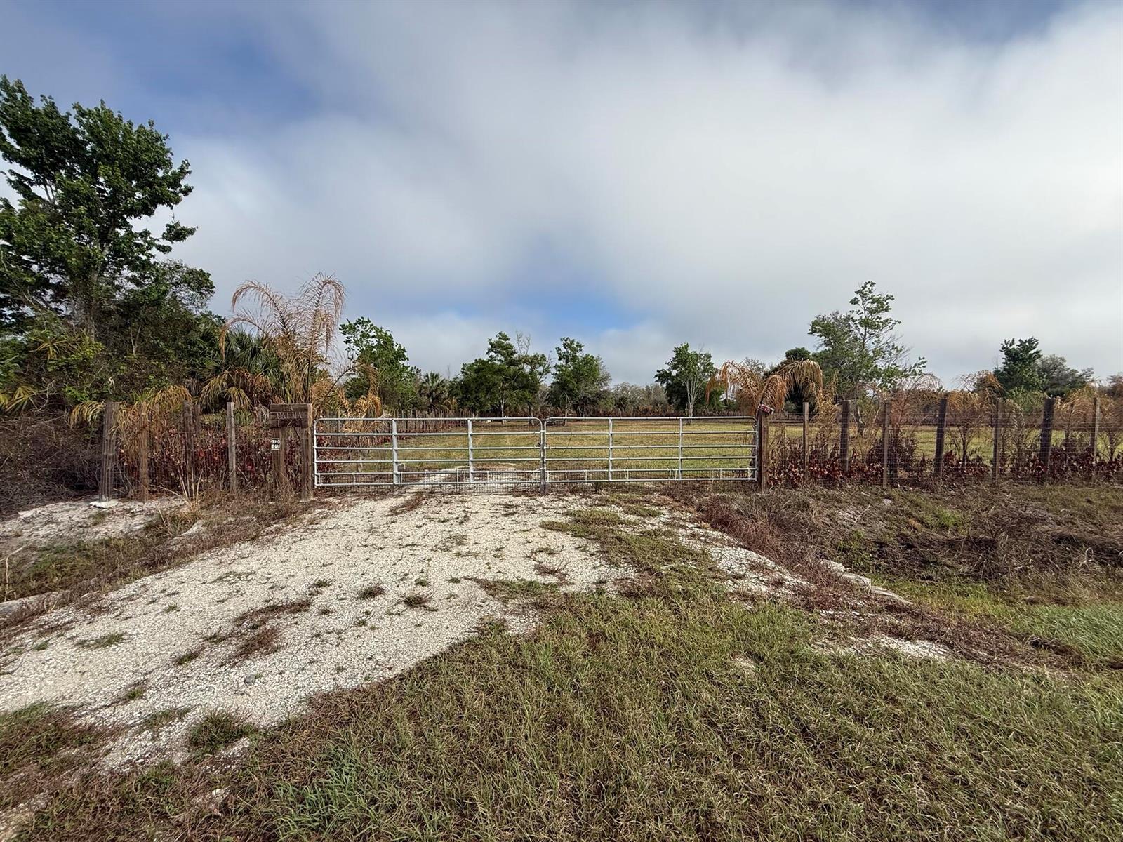 A gravel driveway leads to a metal gate opening into a fenced, grassy field — 17231 NW 268th Street, Okeechobee FL 34972, OKEECHOBEE, FL