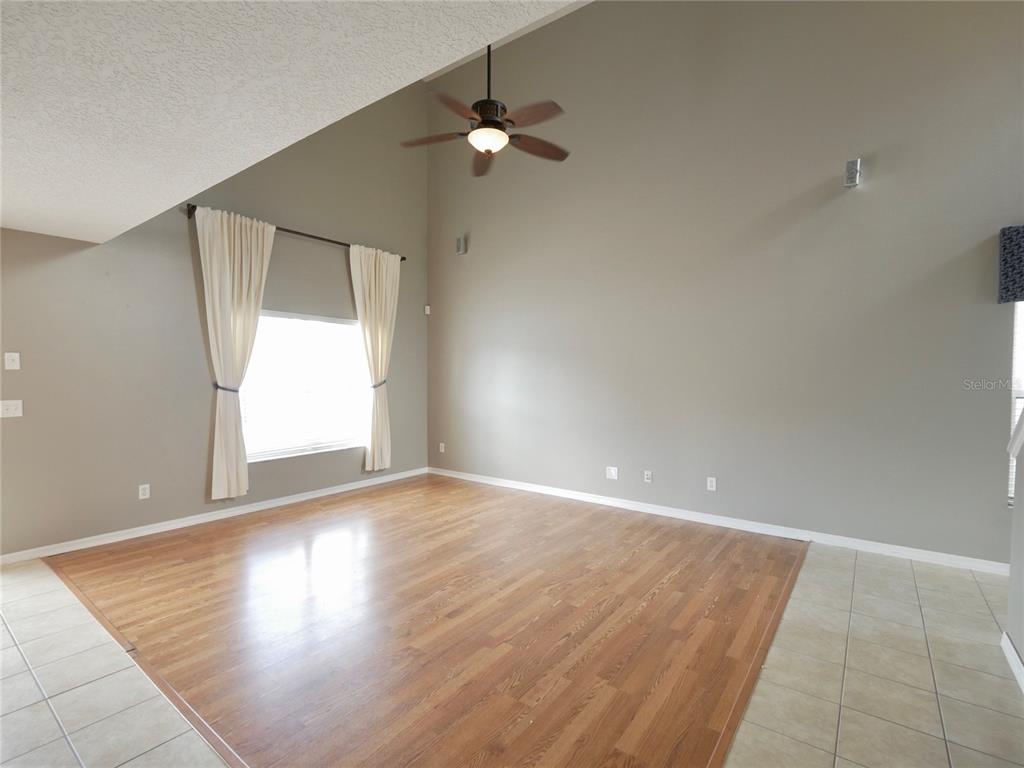 An empty living room features vaulted ceilings, wood flooring, and a ceiling fan — 1914 SHERBOURNE STREET, WINTER GARDEN, FL