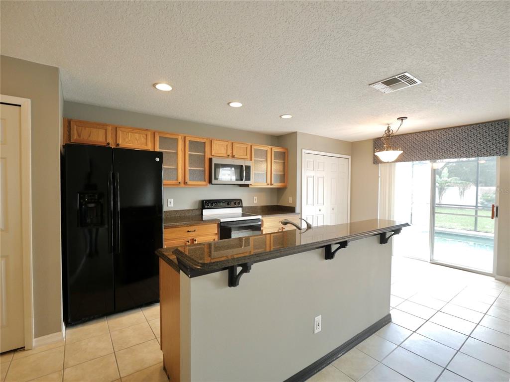 A kitchen with wood cabinets, black appliances, granite countertops, and a breakfast bar — 1914 SHERBOURNE STREET, WINTER GARDEN, FL