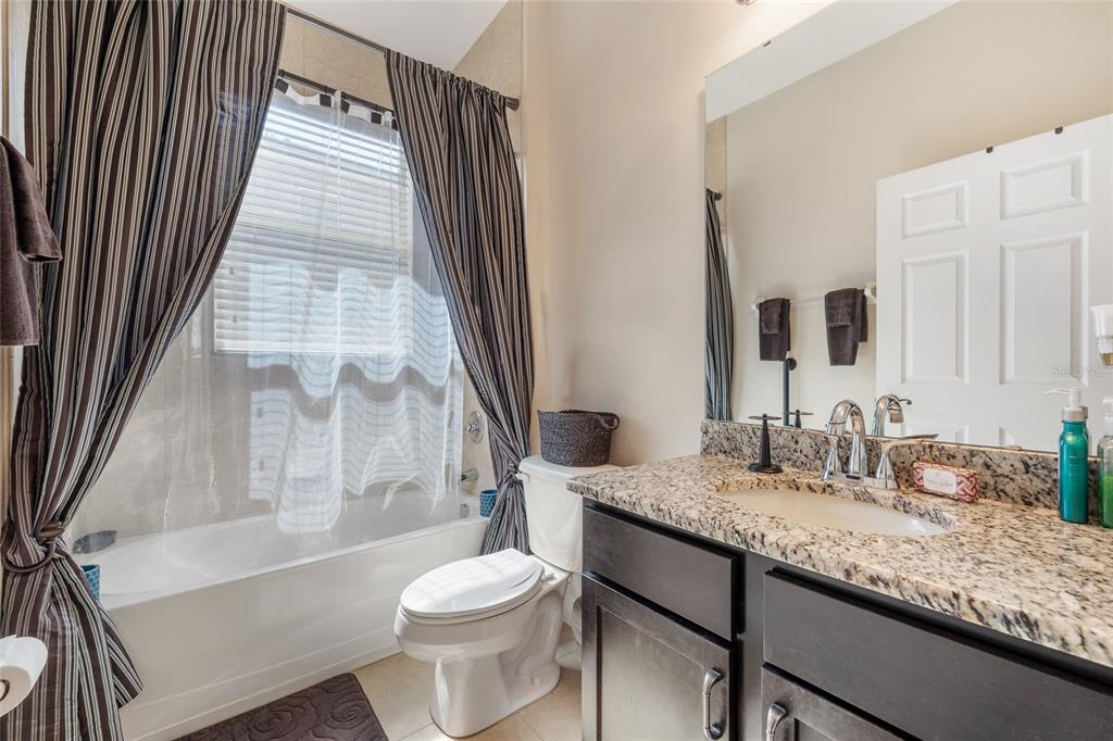A bathroom features a granite vanity, dark wood cabinets, a toilet, and a shower-tub combo — 4436 AZURE ISLE WAY, KISSIMMEE, FL