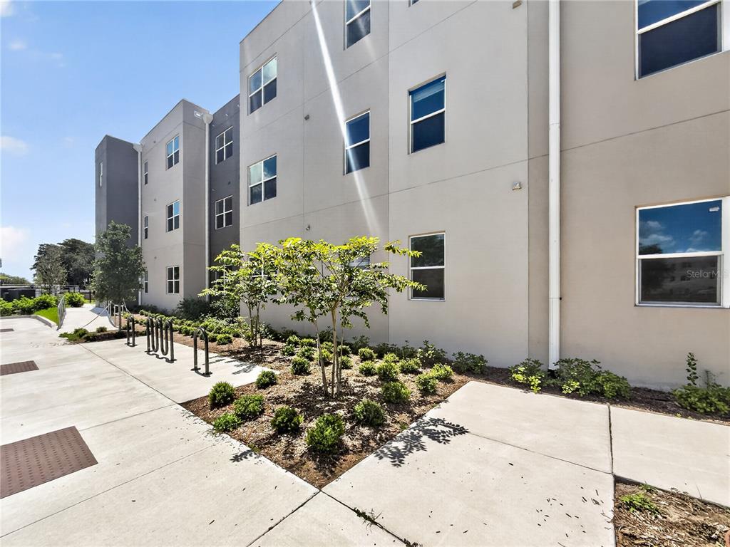 An exterior view of a multi-story apartment building with a landscaped garden and bike racks — 4424 S TEXAS AVENUE UNIT 1-319, ORLANDO, FL