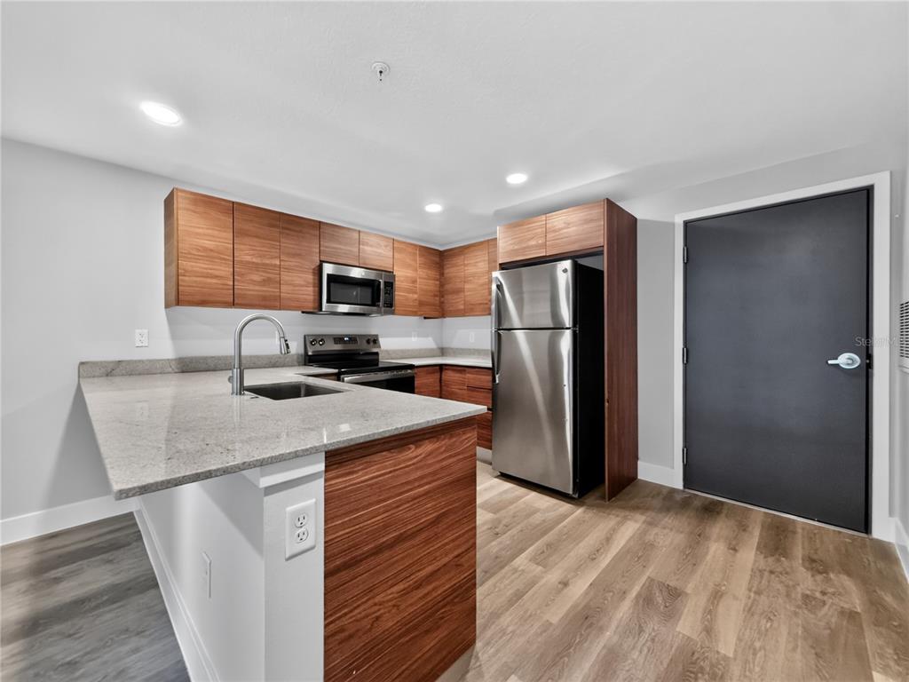 A kitchen features wood-grain cabinets, stainless steel appliances, granite countertops, and light wood flooring — 4424 S TEXAS AVENUE UNIT 1-319, ORLANDO, FL