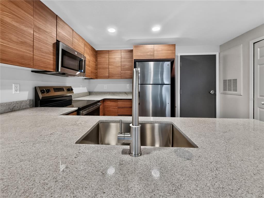 A kitchen features wood-grain cabinets, stainless steel appliances, and a granite countertop with a sink — 4424 S TEXAS AVENUE UNIT 1-319, ORLANDO, FL