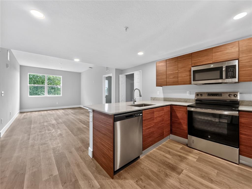 A modern kitchen with wood-grain cabinets and stainless steel appliances opens into a living area — 4424 S TEXAS AVENUE UNIT 1-319, ORLANDO, FL
