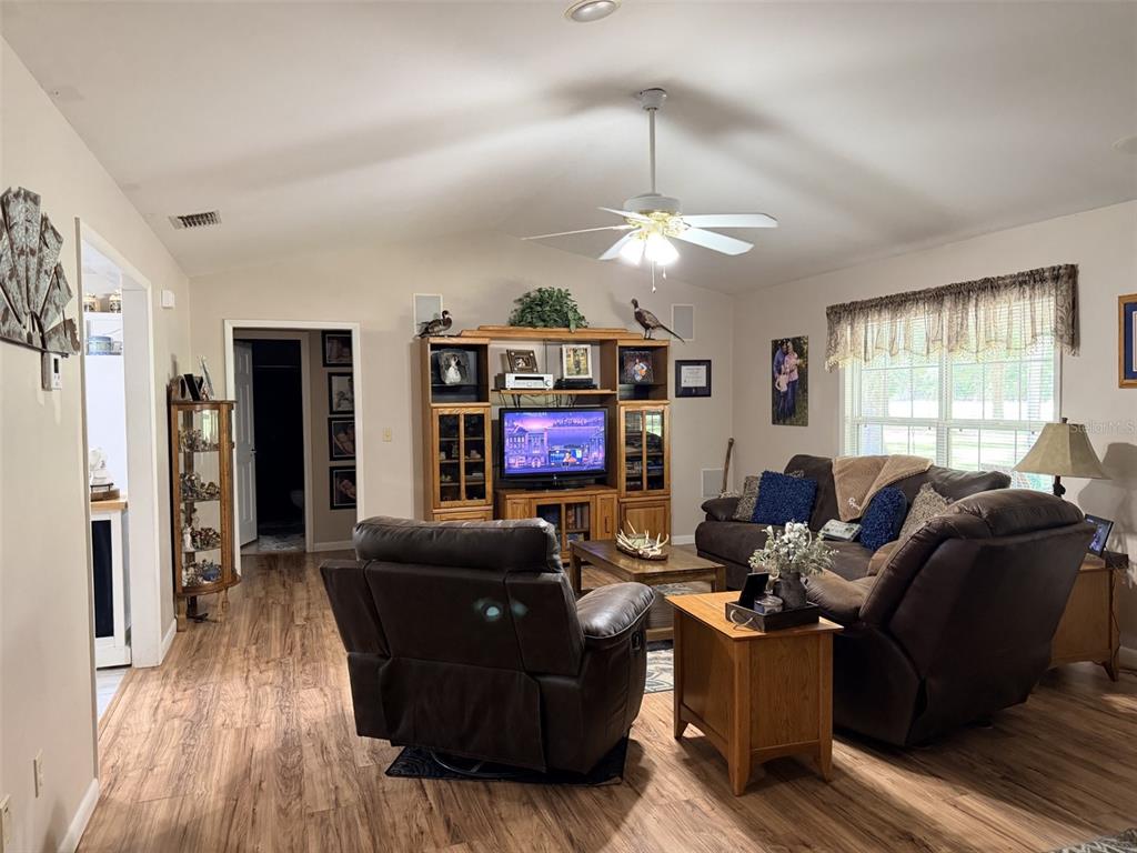A living room features brown leather furniture, a wooden entertainment center, and wood-look flooring — 6051 NW 81ST PLACE, CHIEFLAND, FL