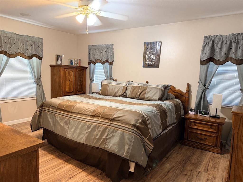 A bedroom features a king-sized bed with brown bedding, wooden furniture, and three windows — 6051 NW 81ST PLACE, CHIEFLAND, FL