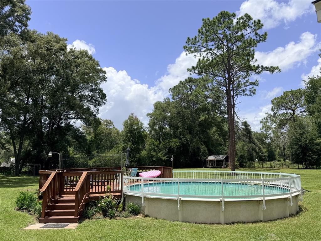 An above-ground swimming pool with a wooden deck and white safety fence in a yard — 6051 NW 81ST PLACE, CHIEFLAND, FL