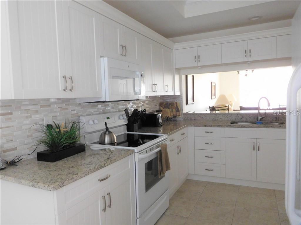 A kitchen with white cabinets, granite countertops, stainless steel appliances, and a tiled backsplash — 8735 OLDE HICKORY AVENUE UNIT 8104, SARASOTA, FL