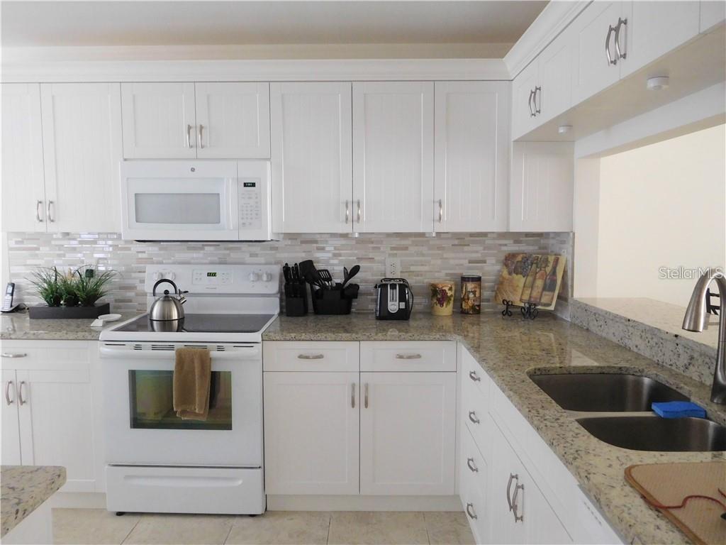 A kitchen with white cabinets, granite countertops, a white stove, and a tile backsplash — 8735 OLDE HICKORY AVENUE UNIT 8104, SARASOTA, FL