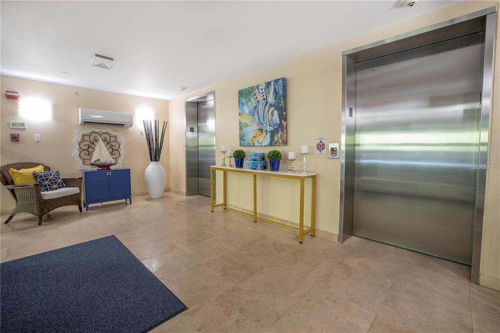 An elevator lobby features tiled floors, a console table, a wicker chair, and wall art — 12077 GANDY BOULEVARD N UNIT 332, ST PETERSBURG, FL