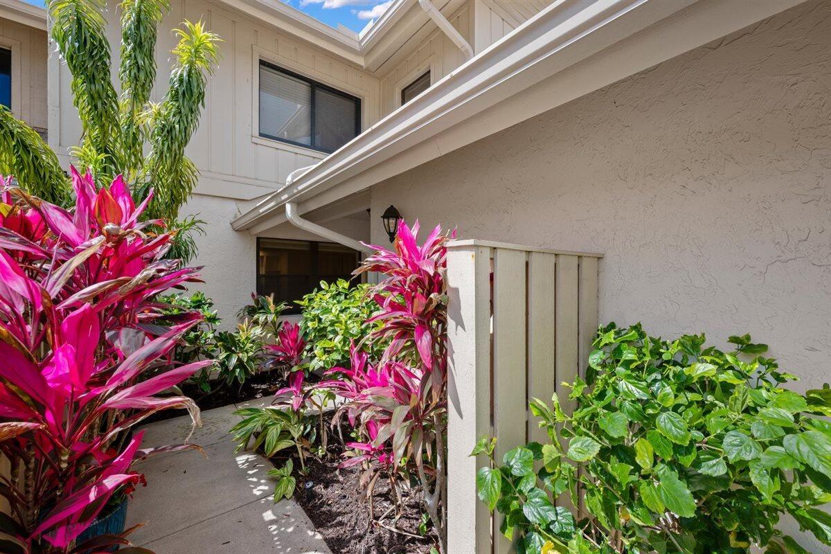 A paved walkway leads to a building entrance surrounded by vibrant pink-leafed plants and greenery — 17138 Waterbend Drive # 117, Jupiter FL 33477, JUPITER, FL