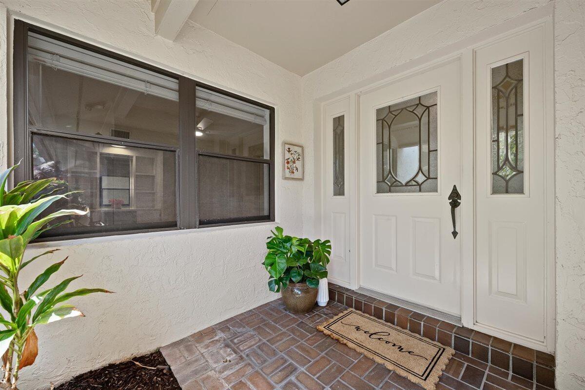 A front entryway features a white door with glass panels, brick flooring, and a plant — 17138 Waterbend Drive # 117, Jupiter FL 33477, JUPITER, FL