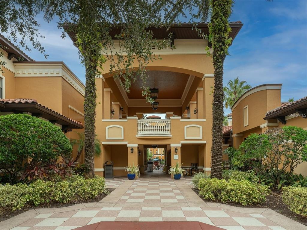 A paved walkway leads to the covered entrance of a Mediterranean-style building with palm trees — 12544 FLORIDAYS RESORT DRIVE UNIT 402B, ORLANDO, FL