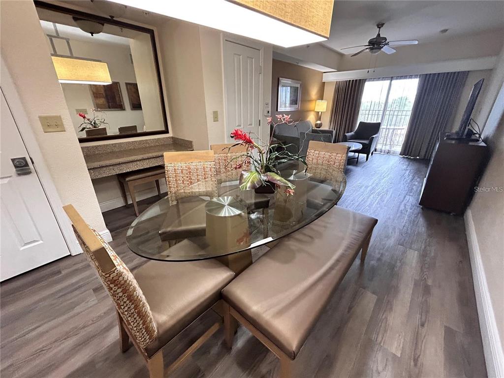 A dining area with a glass table, chairs, and a bench sits near a living space — 12544 FLORIDAYS RESORT DRIVE UNIT 402B, ORLANDO, FL