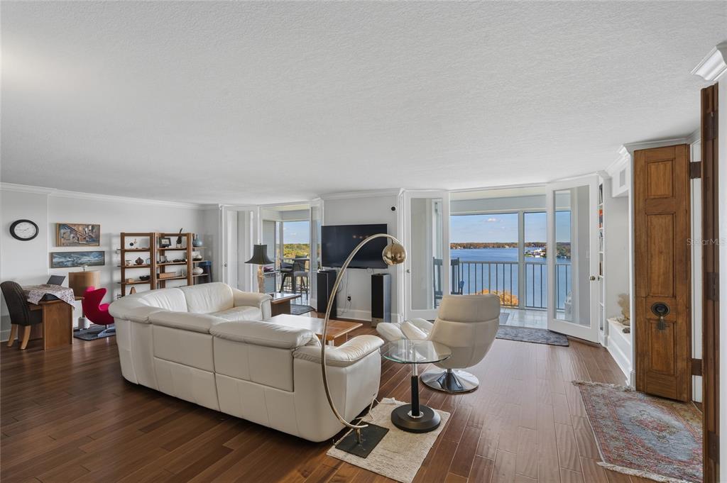 A living room with white leather furniture, hardwood floors, and a balcony overlooking a lake — 1100 S ORLANDO AVENUE UNIT 956, MAITLAND, FL