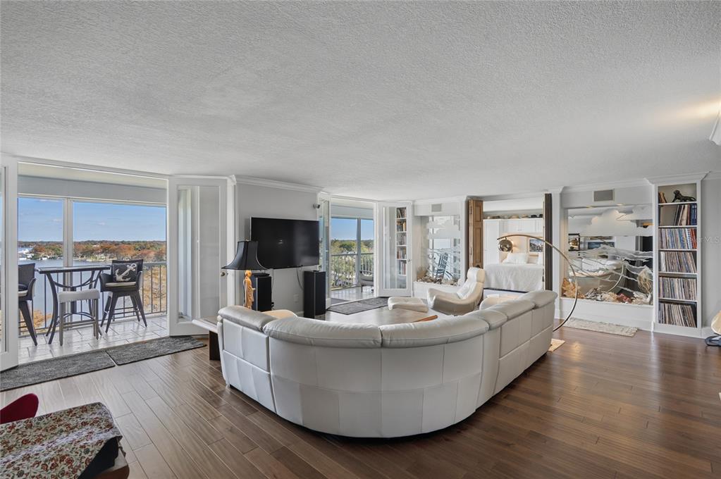 A spacious living room features a white curved sofa, hardwood floors, and a balcony view — 1100 S ORLANDO AVENUE UNIT 956, MAITLAND, FL