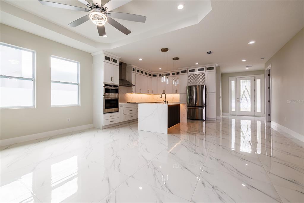 A modern kitchen features white marble floors, white cabinetry, a center island, and stainless appliances — 3803 W PALMETTO STREET, TAMPA, FL