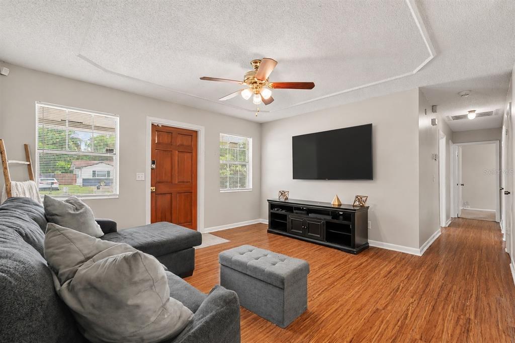 A living room features wood-look flooring, a gray sectional sofa, and a wall-mounted television — 4419 DOLPHIN DR, TAMPA, FL