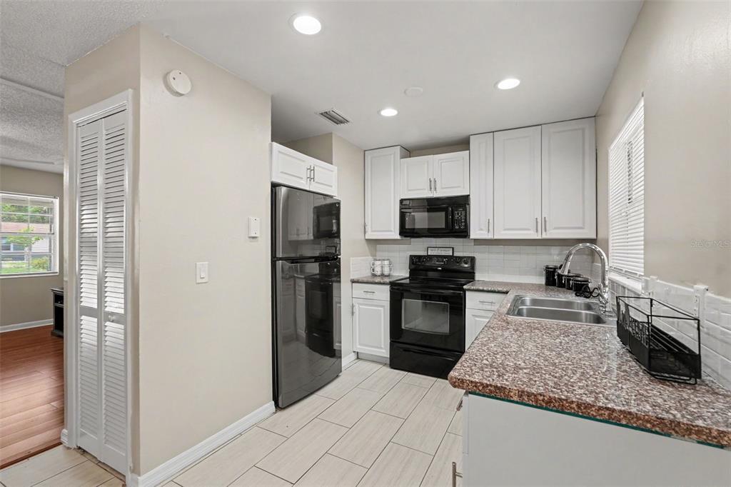 A kitchen features white cabinets, black appliances, granite countertops, and light-colored tile flooring — 4419 DOLPHIN DR, TAMPA, FL