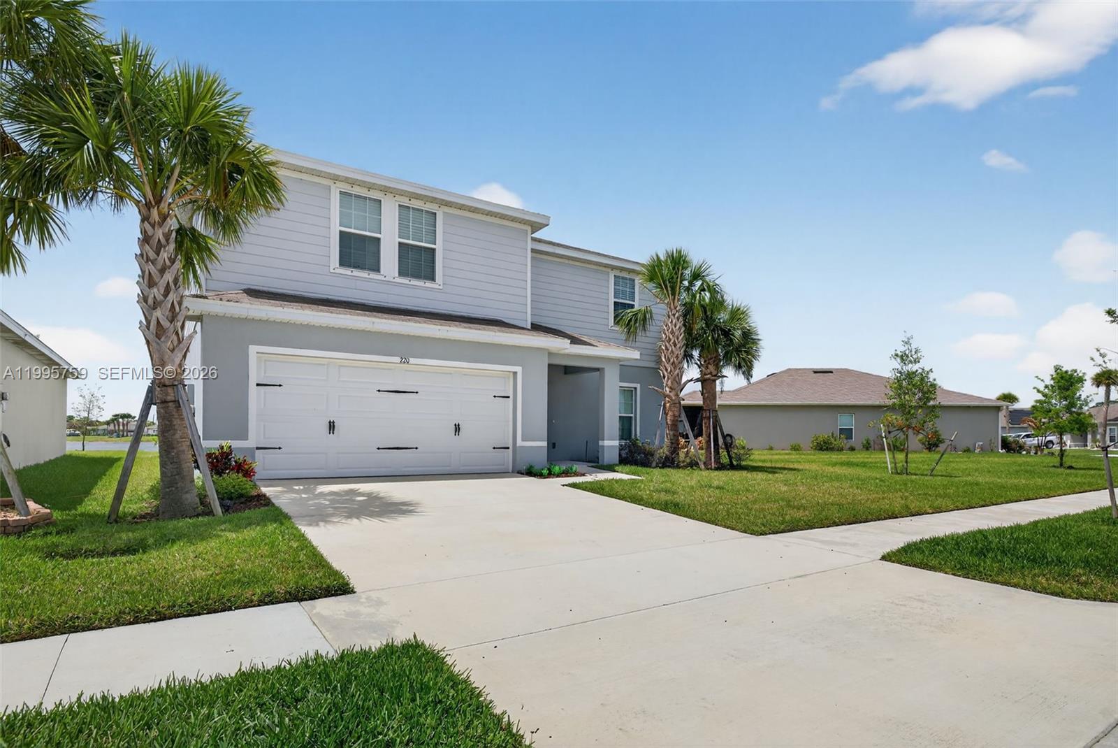 A two-story house with a white garage door, light gray siding, and palm trees — 220 Raspberry Rd, Fort Pierce FL 34981, FORT PIERCE, FL